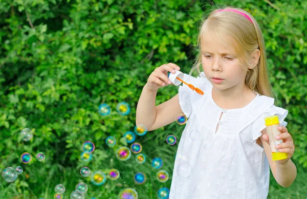 Kleines Mädchen pustet Seifenblasen im Park. — Stockfoto