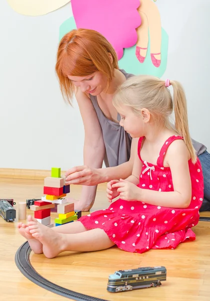 Niña y su madre jugando con el ferrocarril sentado en el suelo . — Foto de Stock