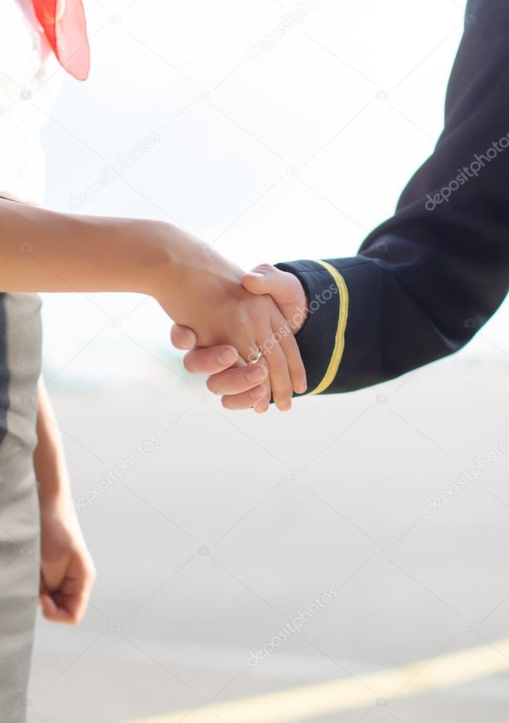 Pilot and stewardess shaking hands on airfield background.