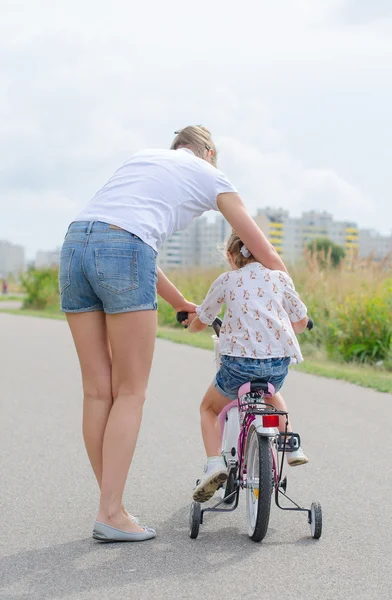 Mujer enseñando a la niña a andar en bicicleta . — Foto de Stock