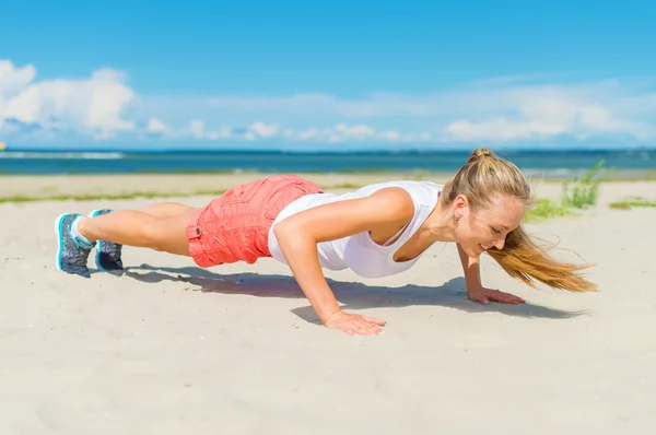 Kvinnan gör armhävningar på stranden. — Stockfoto