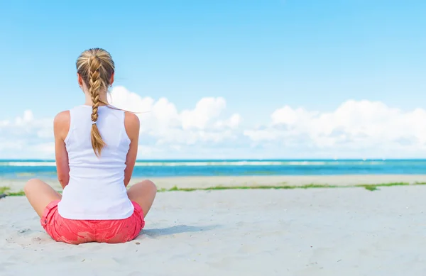 Pigtailed holka sedí na pláži a meditací. — Stock fotografie