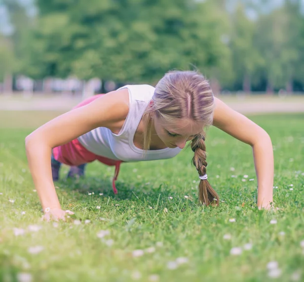 Pretty woman doing push-ups in the park. — Stock Photo, Image