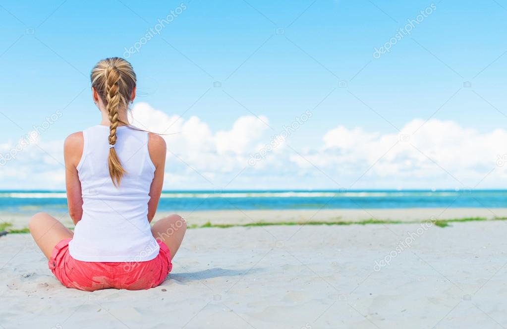 Pigtailed girl sitting on the beach and meditating.