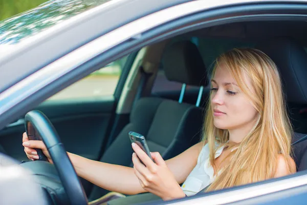 Schöne junge Frau schreibt SMS, während sie Auto fährt. — Stockfoto