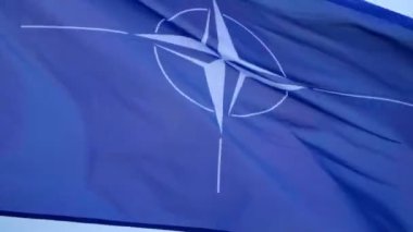 Büyük NATO bayrağı direkte dalgalanıyor.