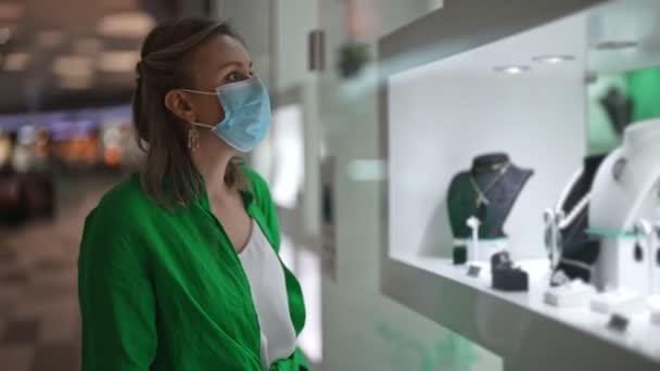 Γυναίκα Στην Ιατρική Μάσκα Κοιτάζει Κοσμήματα Στο Κατάστημα Βιτρίνα — Αρχείο Βίντεο