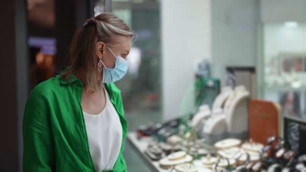 Γυναίκα Στην Ιατρική Μάσκα Κοιτάζει Κοσμήματα Στο Κατάστημα Βιτρίνα — Αρχείο Βίντεο