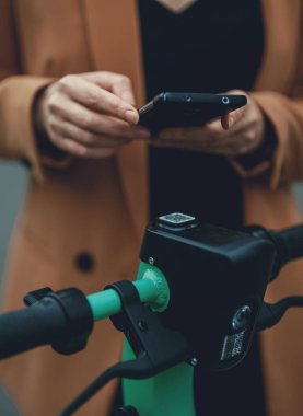 Sokakta elektrikli scooterın kilidini açmak için akıllı telefondaki uygulamayı kullanan kadın..