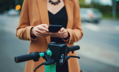 Sokakta elektrikli scooterın kilidini açmak için akıllı telefondaki uygulamayı kullanan kadın..
