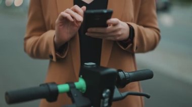 Sokakta elektrikli scooterın kilidini açmak için akıllı telefondaki uygulamayı kullanan kadın..