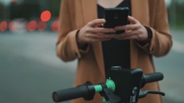 Sokakta elektrikli scooterın kilidini açmak için akıllı telefondaki uygulamayı kullanan kadın..