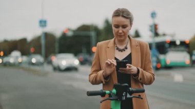 Sokakta elektrikli scooterın kilidini açmak için akıllı telefondaki uygulamayı kullanan kadın..
