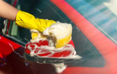 Eldivenli kadın araba aynasını süngerle yıkıyor..