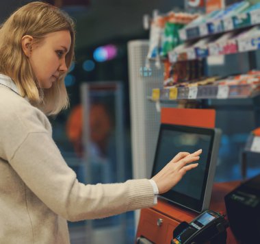 Woman pays at self-checkouts in supermarket.