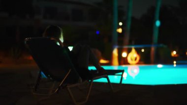 Akıllı telefonlu bir kadın akşam havuz kenarında dinleniyor..