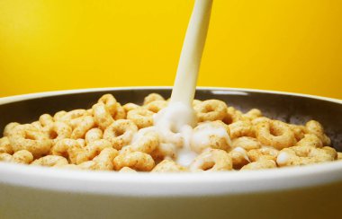 Pouring milk in bowl with round honey cereals.