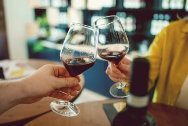 Man and a woman clink glasses of red wine.
