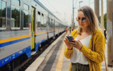 Akıllı telefonlu bir kadın trenini bekliyor..