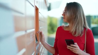 Woman entering code to pickup mail from automated postal machine.