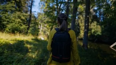 Woman tourist with backpack exploring forest. Back view.