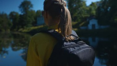 Woman tourist with backpack standing near the lake.