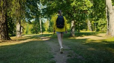 Woman tourist with backpack exploring forest. Back view.