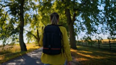 Woman tourist with backpack walking in the countryside. Rear view.