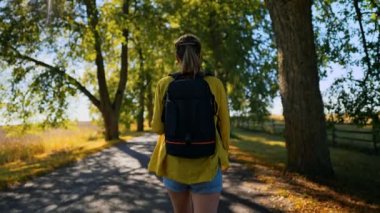 Woman tourist with backpack walking in the countryside. Rear view.