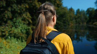 Woman tourist with backpack standing near the lake.