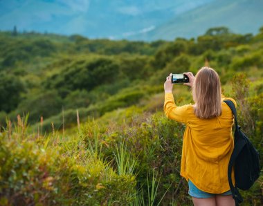 Woman with backpack photographs the mountains at sunset.