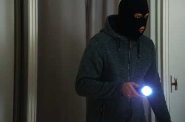 El feneri taşıyan maskeli soyguncu evini kontrol ediyor..