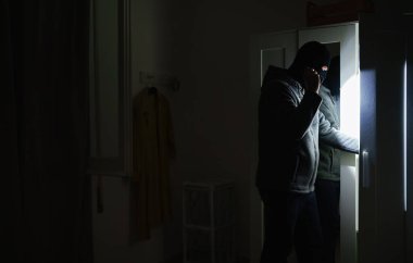 El feneri taşıyan maskeli soyguncu evini kontrol ediyor..