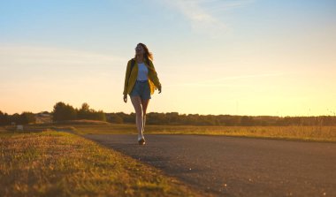 Sırt çantalı bir kadın gün batımında yolda yürüyor..