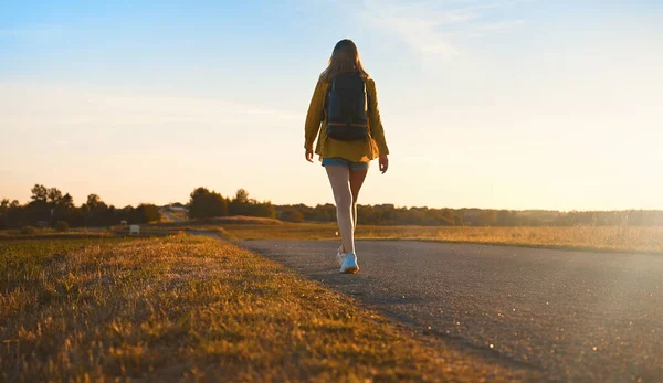 Sırt Çantalı Bir Kadın Gün Batımında Yolda Yürüyor — Stok fotoğraf