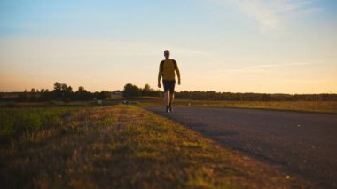 Sırt çantalı bir adam gün batımında yolda yürüyor..