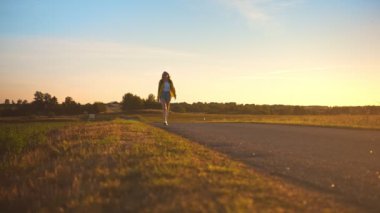 Sırt çantalı bir kadın gün batımında yolda yürüyor..