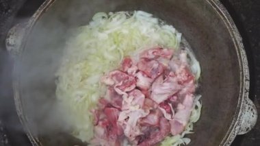 Açık havada ateşte bir kazanda yemek pişirmek. Soğan ve tavuk eti, dökme demir bir kazanda hazırlanır. Hazırlama pilavı