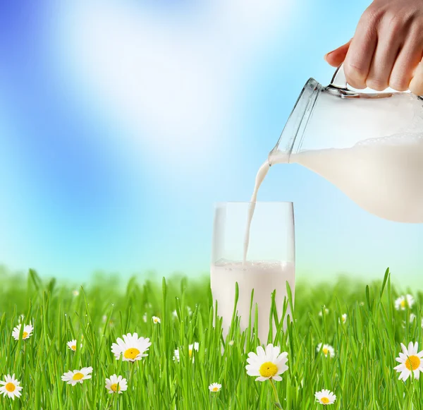 Milk pouring into glass in grass — Stock Photo, Image