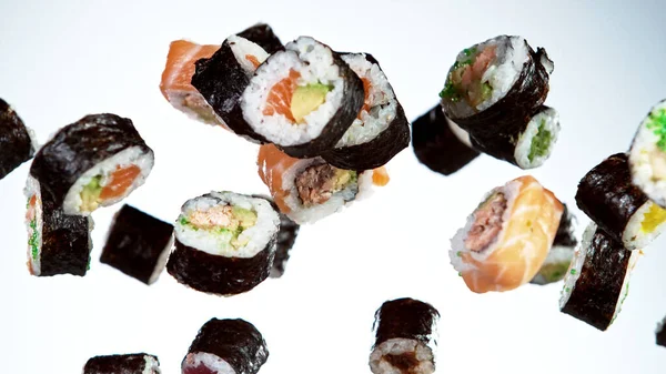 Beyaz arka planda uçan suşi parçalarının hareketlerini dondur. Geleneksel Japon yemeklerini uçurma kavramı. Stüdyo çekimi, koyu arkaplan.