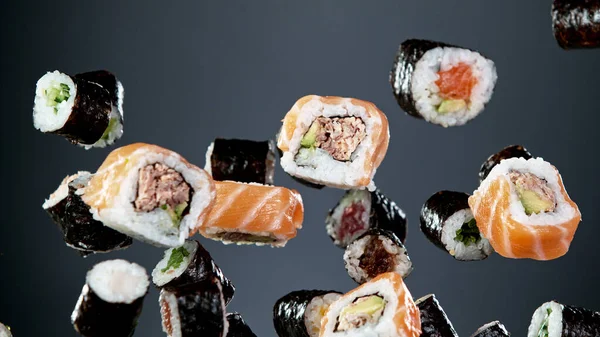 Siyah arka planda uçan suşi parçalarının hareketlerini dondur. Geleneksel Japon yemeklerini uçurma kavramı. Stüdyo çekimi, koyu arkaplan.