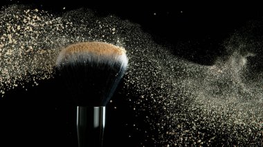 Yumuşak kozmetik fırçası, siyah arka planda fotokopi alanı olan bir bej yüz pudrası bulutu salıyor. Güzellik ve makyaj konsepti