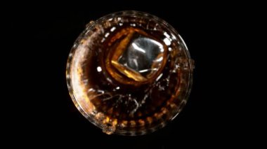 Buz küpünün viskiye dönüşmesi süper yavaş bir hareket, siyah arka plan. Yüksek hızlı sinema kamerası, 1000fps