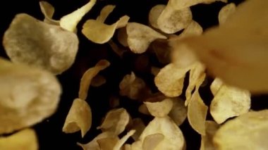 Uçan kızarmış patates cipslerinin süper yavaş çekimi, geniş makro çekim. Hız rampası etkisi. Siyah arka planda izole edilmiş. Yüksek hızlı sinema kamerası, 1000 fps..