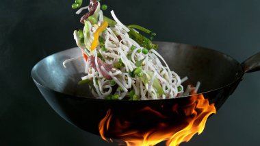 Şefin tavadaki tavadan Asya eriştesi karışımı ile biftek parçaları fırlatmasına yakın çekim. Koyu arkaplanda taze Asya yemeği hazırlığı.