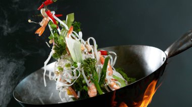 Şef 'in tavadan karides fırlatmasına yakın çekim. Koyu arkaplanda taze Asya yemeği hazırlığı.