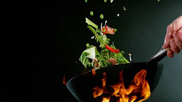 シェフのクローズアップ火に鍋からアジアミックスとサーモン作品をスローします 暗い背景に新鮮なアジア料理の準備 — ストック写真