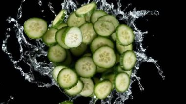 Süper yavaş çekimde salatalık dilimleri su ile dönüyor, siyah arkaplan. Yüksek hızlı sinema kamerası, 1000 fps. Hız rampası etkisi.