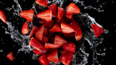 Su sıçratan ve siyah arka planda dönen çileklerin süper yavaş çekimleri. Yüksek hızlı sinema kamerası, 1000 fps. Hız rampası etkisi.