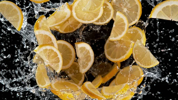 水のスプラッシュでスライスされたレモンの動きを凍結します 黒の背景に隔離 — ストック写真